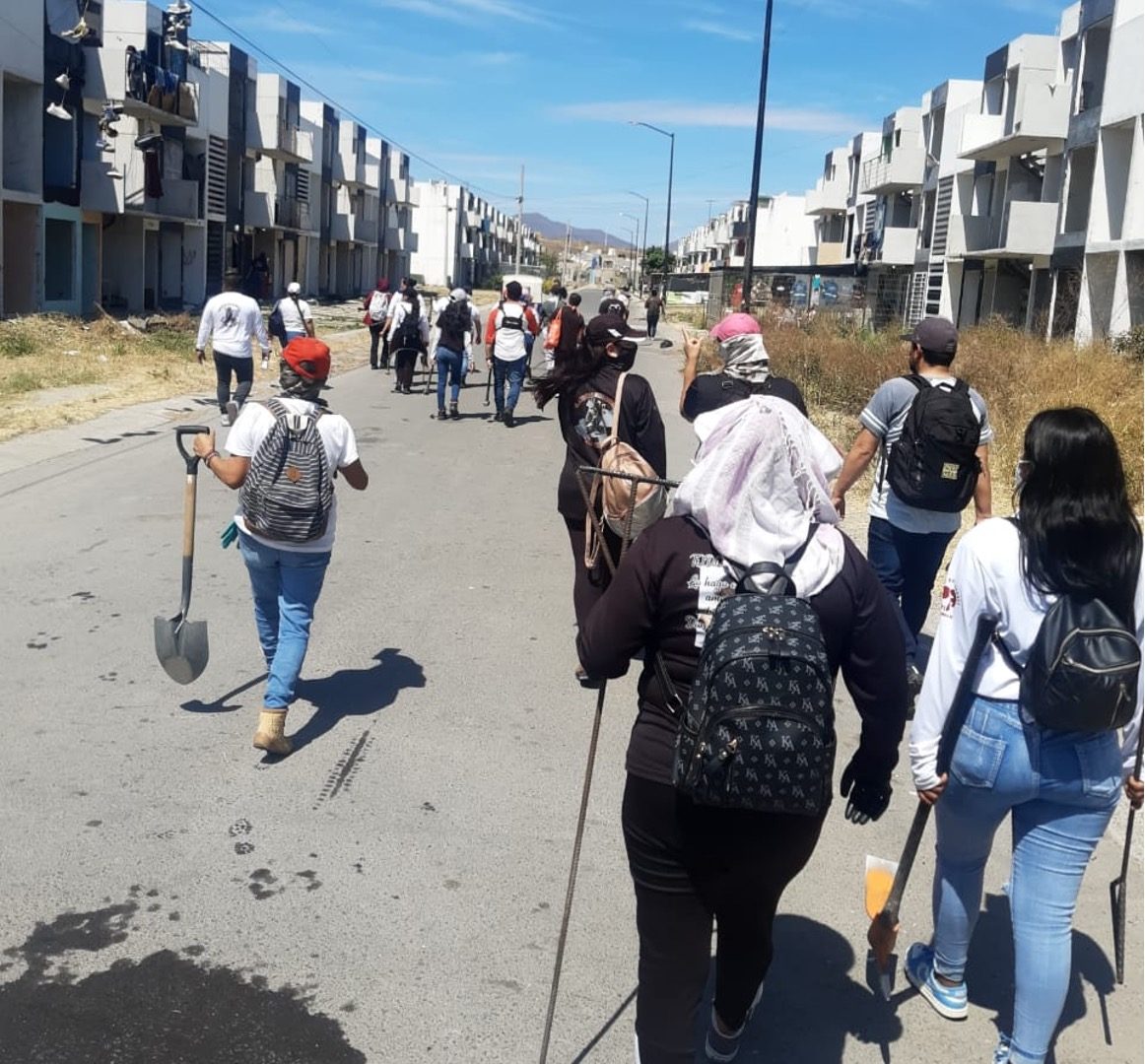 A search collective walking down a street of abandoned houses carrying shovels and probes